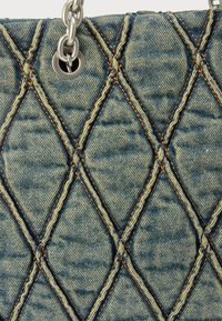 Borsa in denim trapuntato con motivo a diamante, caratterizzata da cuciture arancioni a contrasto e tracolla a catena argentata con dettaglio hardware circolare.