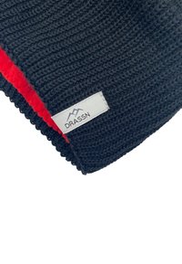 Black knitted beanie with a soft red lining, featuring a white label reading "DRASSN." The texture is ribbed with a scalloped edge.