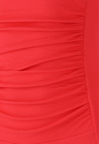 Röd texturerad tyg med samlade veck, med ett honungskake-mönster och släta områden. Materialet ser flexibelt och åtsittande ut.
