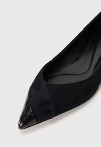 Ballerines noires à bout pointu avec un dessus en suede et un bout en cuir laqué. L'intérieur présente une doublure noire lisse et une semelle intérieure moulée.