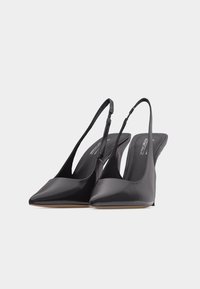 Escarpins noirs à bout pointu avec bride arrière, fines lanières et talon stiletto bas sur fond blanc.