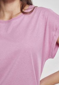 Camiseta de manga corta color rosa claro con cuello redondo, textura suave y corte relajado. Costuras visibles a lo largo del cuello y las mangas.
