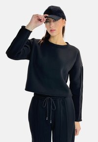Felpa nera corta con maniche lunghe, abbinata a joggers neri a coste con vita elastica. Entrambi realizzati in tessuto morbido; incluso un berretto alla moda.