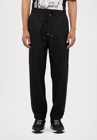 Black sweatpants with a drawstring waistband, featuring side pockets and tapered cuffs. The fabric is smooth and lightweight.