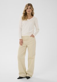 Cream long-sleeve v-neck top with scalloped hems paired with light beige wide-leg pants featuring scattered black polka dots and pockets.