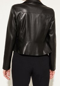 Veste en cuir noir à la coupe structurée, avec un ourlet peplum et des coutures visibles, vue de dos. Texture lisse.