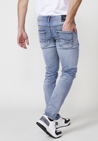 Svetlomodré džínsy s úzkym strihom, majúce dve zadné vrecká s dekoratívnym stehmi a značku na páse. Nosené s bielymi a čiernymi teniskami.