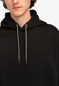 Felpa nera con cappuccio realizzata in tessuto morbido, con un logo frontale in una finitura discreta e lacci multicolori con punte metalliche.
