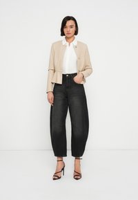 Μπεζ cropped σακάκι με κουμπιά, λευκό πουκάμισο από μέσα και τζιν παντελόνι ψηλόμεσο, σε σκούρο μπλε χρώμα με φαρδιά μπατζάκια, συνδυασμένο με μαύρα πέδιλα με λουράκια.