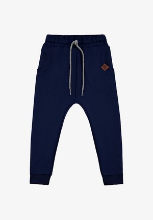Granatowe dziecięce spodnie dresowe z elastycznym paskiem, paskowanym sznurkiem, przednimi kieszeniami, ściągaczami na końcach nogawek oraz małą brązową metką z logo.