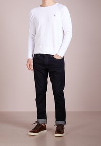 Vit crewneck-tröja med ribbstickade muddar, kombinerad med mörka denimjeans och bruna snörskor. Enkel design och avslappnad passform.