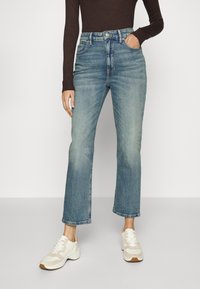 Ljust blå denimjeans med rak passform, hög midja och subtila slitningar. Kombineras med vita sneakers med beige detaljer.