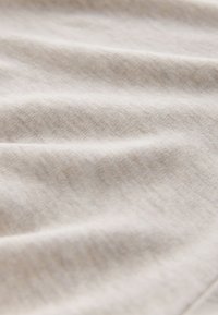 Tissu beige doux avec des plis subtils et une fine texture tricotée visible de près.