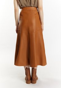 Woman wearing a high-waisted, A-line brown leather midi skirt paired with matching brown ankle boots, shown from the back.