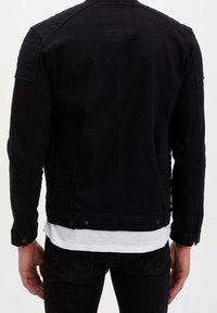 Czarna kurtka motocyklowa z denimu z pikowanymi akcentami na ramionach, zatrzaskami i dopasowanym krojem. Widok od tyłu podkreśla detale przeszyć.