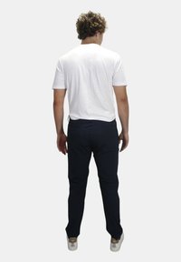 Witte short-sleeve t-shirt gecombineerd met donkerblauwe broek, met een slim fit en casual sneakers met tan accenten, gezien van achteren.