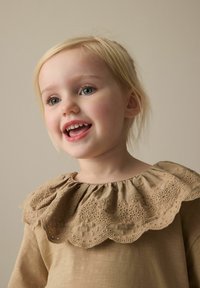Tan bomulls topp med scalloped, broderad krage med blommiga detaljer, korta ärmar och en mjuk, texturerad yta.