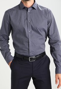 Rutig knäppskjorta i marinblått och vitt, med klassisk krage, långa ärmar och bröstficka; kombinerat med mörka byxor.