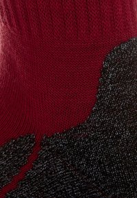 Calcetines de punto con una sección superior de un rojo profundo y un patrón texturizado negro en la base, hechos de un material suave y elástico.