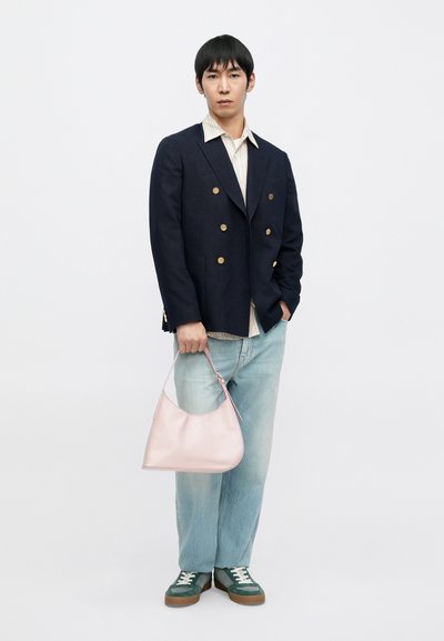 Granatowa marynarka dwurzędowa, koszula w paski, jasne dżinsy. Trzyma gładką, jasnoróżową skórzaną torebkę na ramię. Zielone trampki z białymi sznurowadłami.