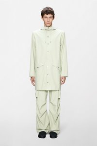 Ανοιχτό πράσινο, αδιάβροχο αδιάβροχο με κουκούλα, κουμπιά κλειδώματος και δύο εμπρόσθιες τσέπες· συνδυασμένο με αντίστοιχο παντελόνι με άνετη εφαρμογή και μαύρα υποδήματα.