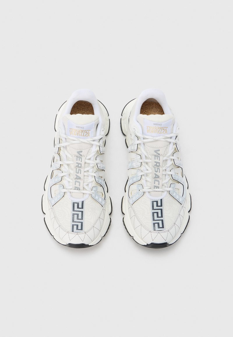 White sneakers with textured design, featuring silver accents, black sole, prominent Versace logo, and Greek pattern on the side.