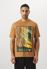 Smeđi pamučni majica s grafičkim printom drveća i tekstom "Chicago Bulls", snažne kontraste boja, kratkim rukavima i opuštenim krojem.