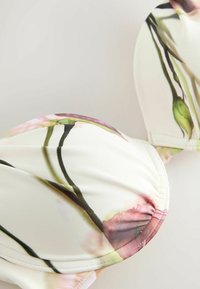 Primo piano di coppe imbottite di reggiseno con tessuto bianco che presenta un delicato motivo floreale rosa e verde.