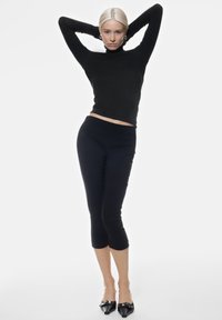 Maglione aderente nero con collo alto e leggings cropped in tessuto liscio. Abbinato a tacchi neri a punta con accenti argentati.