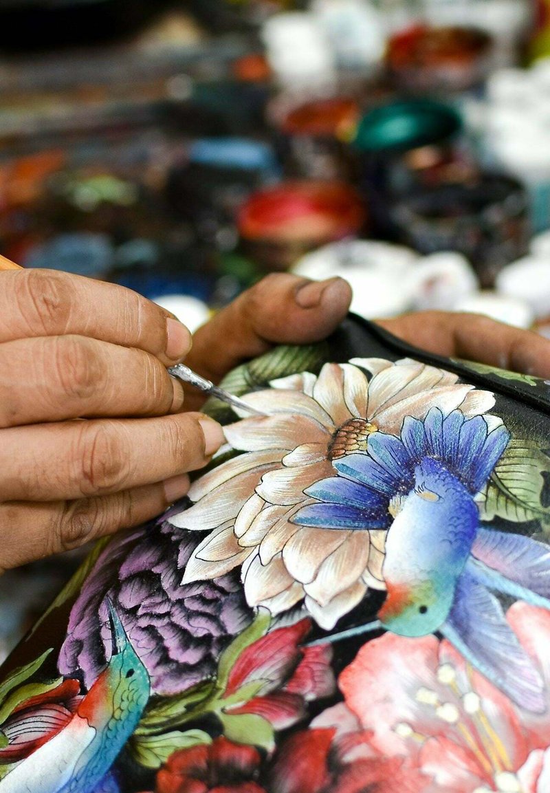 Handgeschilderd op een donkere achtergrond met kleurrijke bloemen, gedetailleerde kolibries en ingewikkelde ontwerpen. Gereedschap en verfpotten op de achtergrond.
