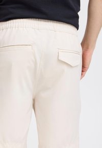 Pantalones beige claros con cintura elástica, que cuentan con dos bolsillos traseros. La tela parece suave y tiene un corte relajado.