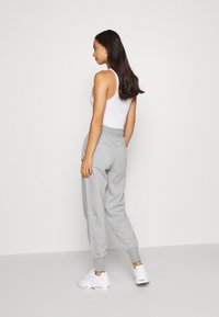 Graue Baumwoll-Jogginghosen mit elastischem Bund, Bündchen an den Knöcheln, seitlichen Taschen, kombiniert mit einem weißen Tanktop und weißen Sneakers.