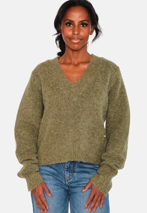 Olivgrön, oversized stickad tröja med V-ringning, ribbade muddar och fåll. Mjuk textur och hela ärmar, parat med blå denimjeans.