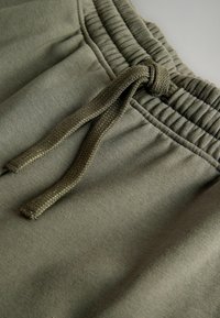 Grüne Jogging-Shorts bestehen aus einem weichen, strukturierten Stoff, einem elastischen Bund und einer geflochtenen Kordel mit einem Knoten vorne.