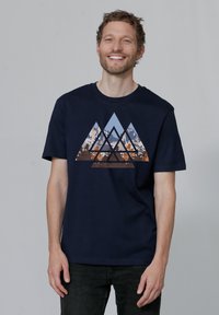 T-shirt en coton bleu marine présentant un graphique de triangles superposés dans des tons de bleu et de terre, illustrant un paysage montagneux.