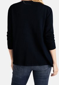 Maglione nero a maniche lunghe con scollo rotondo, texture morbida e vestibilità rilassata; abbinato a jeans in denim scuro.