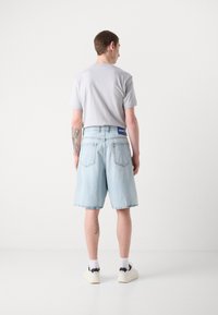 Shorts en denim bleu clair avec une coupe ample, un ourlet effiloché notable et deux poches arrière. Associés à un t-shirt gris et des baskets noires.