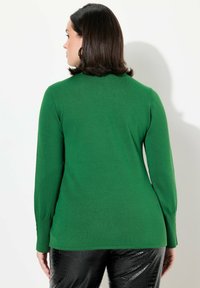 Pull vert à manches longues avec une texture côtelée et une coupe ajustée, associé à un pantalon noir en simili-cuir avec motif serpent brillant. Aucune motif ou accent visible.