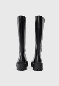 Čierne vysoké čižmy vyrobené z hladkej kože s blokovým podpätkom a robustnou podrážkou. Majú štýlový dizajn s zadným zipsom.