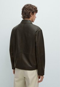 Brown leather jacket with a structured design, featuring a collar and seams. The back shows a clean finish with a slight sheen.