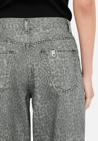 Grijze denim jeans met een subtiele dierenprint, voorzien van twee achterzakken en een metalen label op de rechterzak.