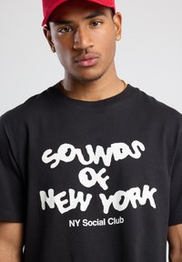 Black cotton t-shirt featuring bold white text "SOUNDS OF NEW YORK" and "NY Social Club." Short sleeves and crew neck design.