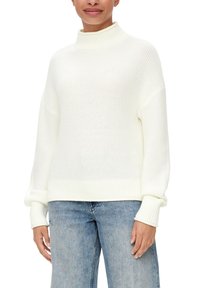 Biały sweter z dzianiny o wysokim kołnierzu i prążkowanymi mankietami. Tekstura jest luźno pleciona, co nadaje mu miękki wygląd. Uzupełniony jasnoniebieskimi dżinsami.