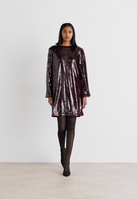 Sequinové šaty v tmavej burgundskej farbe, dlhé rukávy, okrúhly výstrih, po kolená, hladká textura, lesklý povrch, kombinované s čiernymi pančuchami a opätkami.