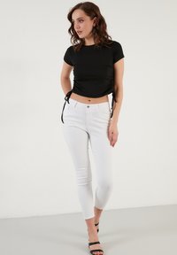 Zwarte geribbelde crop top met korte mouwen, gecombineerd met witte skinny jeans. Beide hebben een aansluitend ontwerp en minimale hardware details.