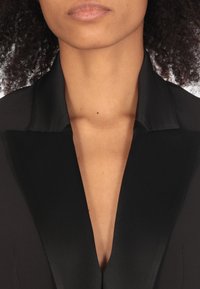 Blazer nero con colletto satinato, scollatura a V profonda e texture liscia. Tessuto di alta qualità con linee pulite e vestibilità su misura.