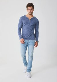 Pikkade varrukatega sinine melange-särk, millel on henley-kaelus ja kolm nööpi, kombineeritud helesiniste teksade ja valgete spordijalanõudega.