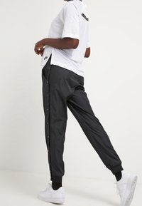 Black button-up athletic pants with elastic cuffs, paired with a white short-sleeve shirt featuring a black accent and logo. White sneakers.