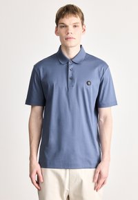 Modré polo tričko z bavlny, s klasick�ým golierom, zapínaním na tri gombíky, krátkymi rukávmi a malou nášivkou s logom na hrudi.