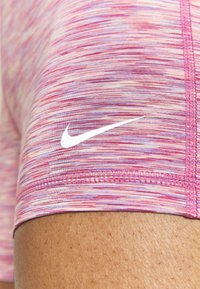 Zbliżenie na udo osoby noszącej różowe, purpurowe i białe wzorzyste spodenki sportowe z białym logo Nike.